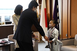 写真：教育長から鰺坂さんにざまりんメダルを渡している