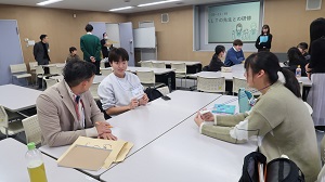 男性の国際親善大使と女性の国際親善大使が外国語指導助手（ALT）を交えて3人で会話をしている様子