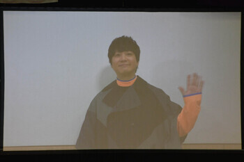 写真：はやしゆうさんビデオメッセージの一場面。カメラに向かって手を振るはやしゆうさん。