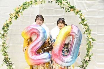 写真：20の形の風船を持って記念撮影をする振袖姿の女性2人