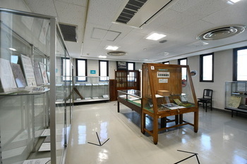写真：常設展示室内の様子。座間にまつわる資料が展示されており、床には順路を示す矢印が書かれています。