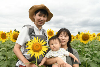 写真：座間会場のヒマワリを背景に親子連れが切り花を持っている様子