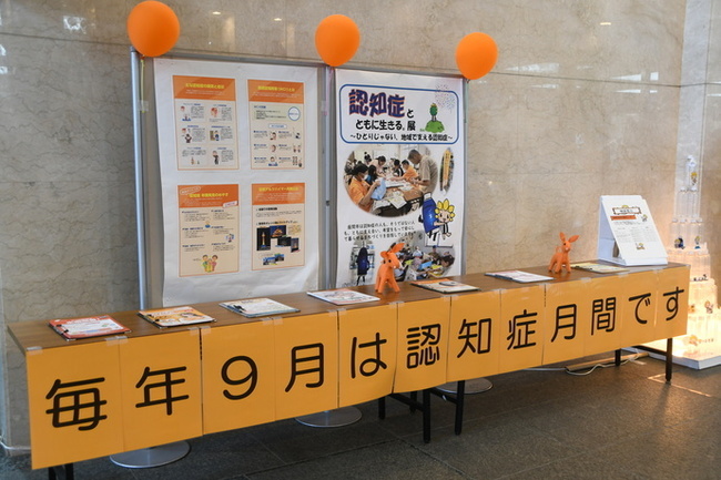 写真：壁には認知症に関するパネルが展示されており、各種パンフレットが展示されているテーブルに「毎年9月は認知症月間です」と書かれた紙が貼ってあります。