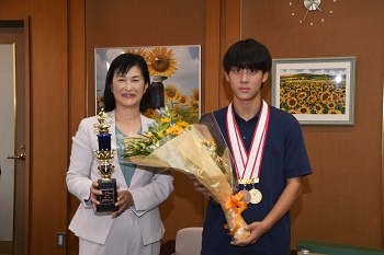 トロフィーを持つ市長と花束を持つ かいだ まさゆき さん